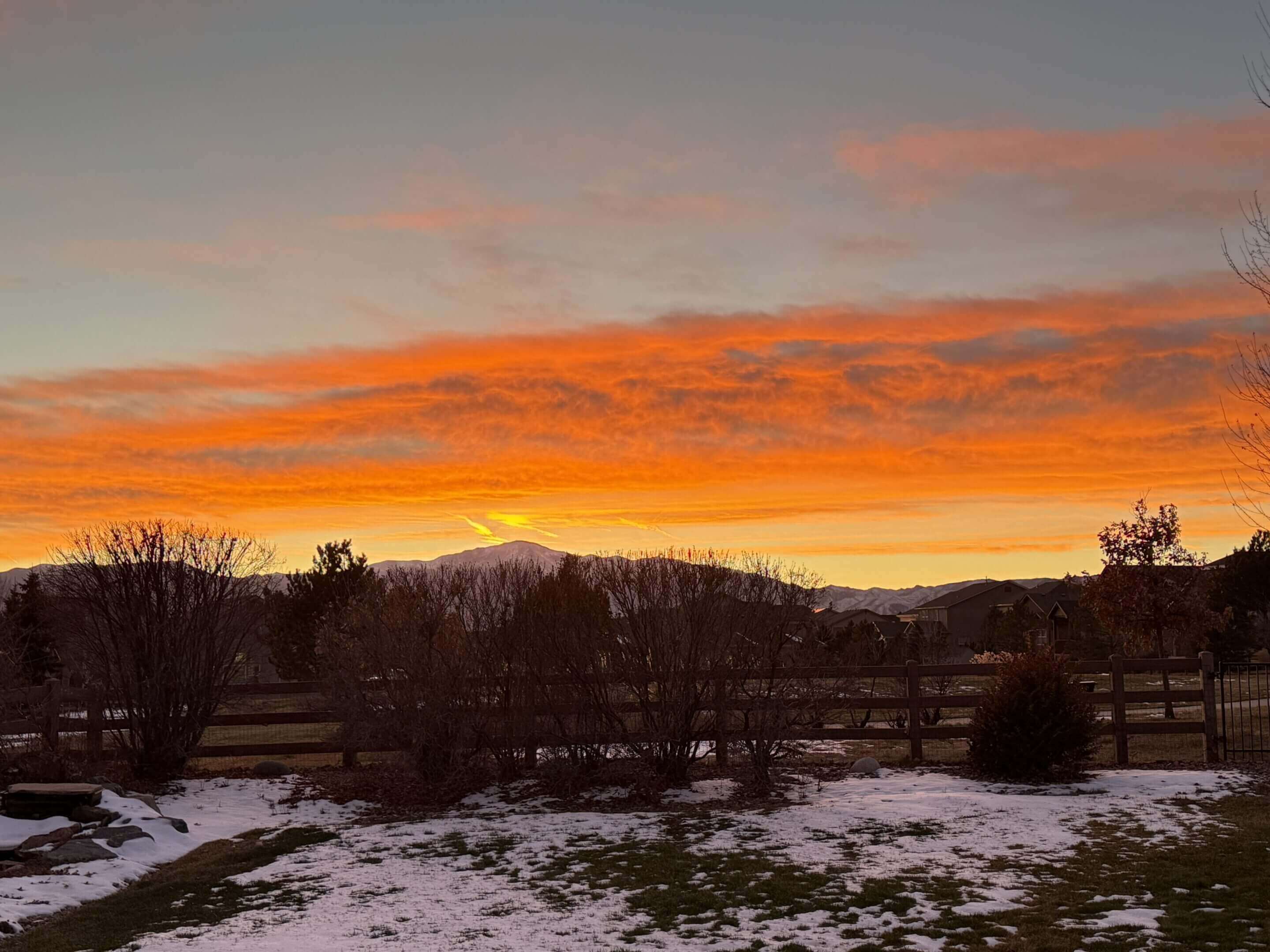Sunset over snowy landscape with orange sky.
